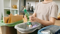 A woman recycles different packaging into different trash cans.  A woman recycles different packaging into different trash cans.