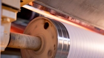 A close-up of a spinning metal roller guiding white fabric through a manufacturing machine.