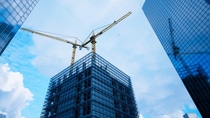 Dynamic view of a towering yellow construction crane rising high at a bustling urban site, set against a vivid blue sky and encircled by imposing glass skyscrapers. Dynamic view of a towering yellow construction crane rising high at a bustling urban site, set against a vivid blue sky and encircled by imposing glass skyscrapers.