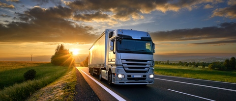 Truck driving on the asphalt road in rural landscape at sunset with dark clouds