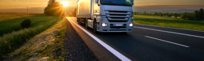 Truck driving on the asphalt road in rural landscape at sunset with dark clouds