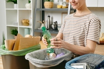 A woman recycles different packaging into different trash cans.  A woman recycles different packaging into different trash cans.